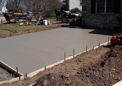 Freshly poured concrete patio next to a house, with construction tools and equipment nearby.