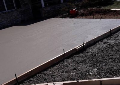 Freshly poured concrete driveway with wooden framing beside a gravel area in front of a house.
