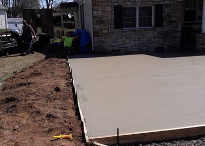 Freshly poured concrete patio in front of a house, with workers and construction equipment nearby.