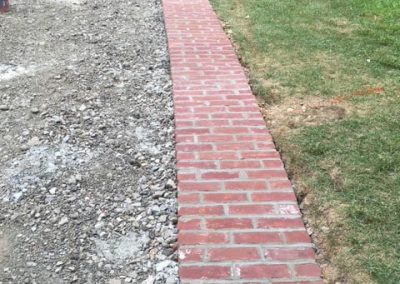 A newly laid brick walkway curves through a yard where construction work is still in progress.