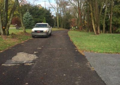 A white pickup truck parked on a paved road lined with trees and patches of grass on a cloudy day.