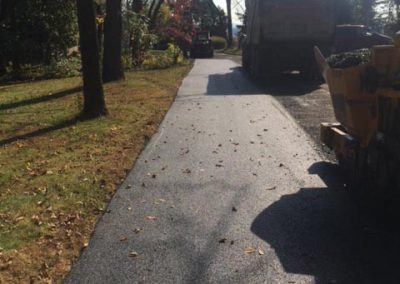 Freshly paved asphalt path beside a grassy area with trees and construction vehicles nearby.