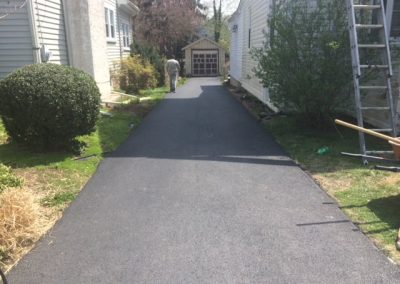 Freshly paved driveway between two houses, leading to a garage; person seen working near the garage.