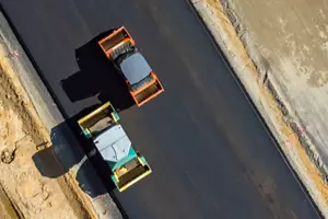 Aerial view of two steamrollers paving a new road with fresh asphalt.