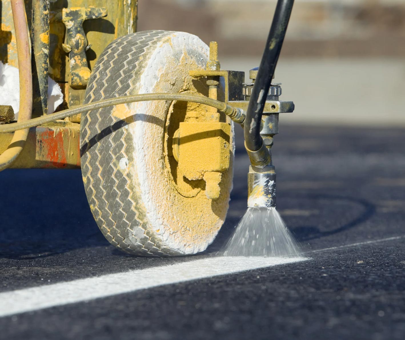 Close-up of a machine painting a white line on asphalt pavement with a spray nozzle.