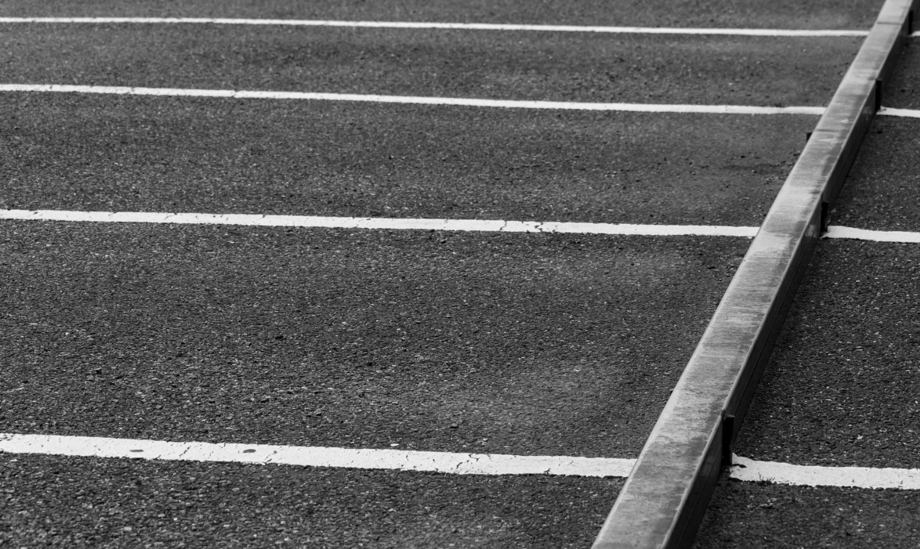 Black and white photo of an empty parking lot with white lines and a concrete barrier diagonally across.