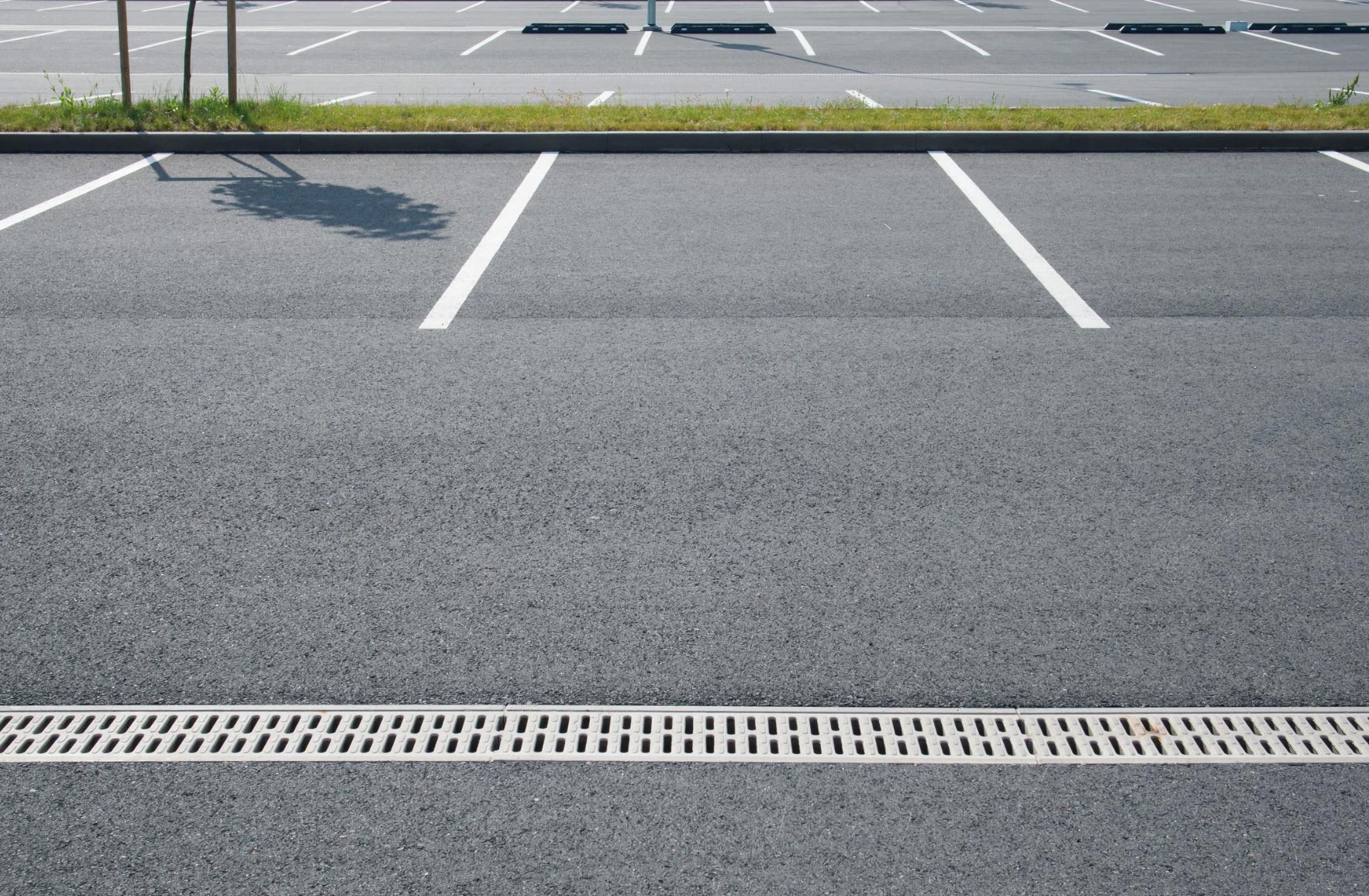 Empty parking spaces in a clean, outdoor parking lot with clear white lines and a metal drainage grate.