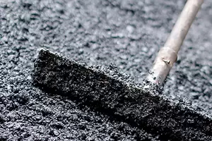 A metal rake spreading fresh asphalt on a road surface.