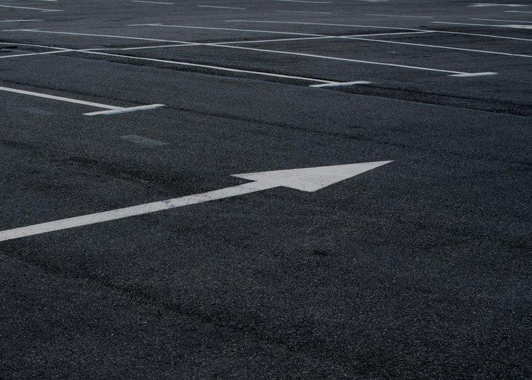 Empty parking lot with crisp line striping, featuring white lines and a large white arrow painted on the asphalt pointing forward.