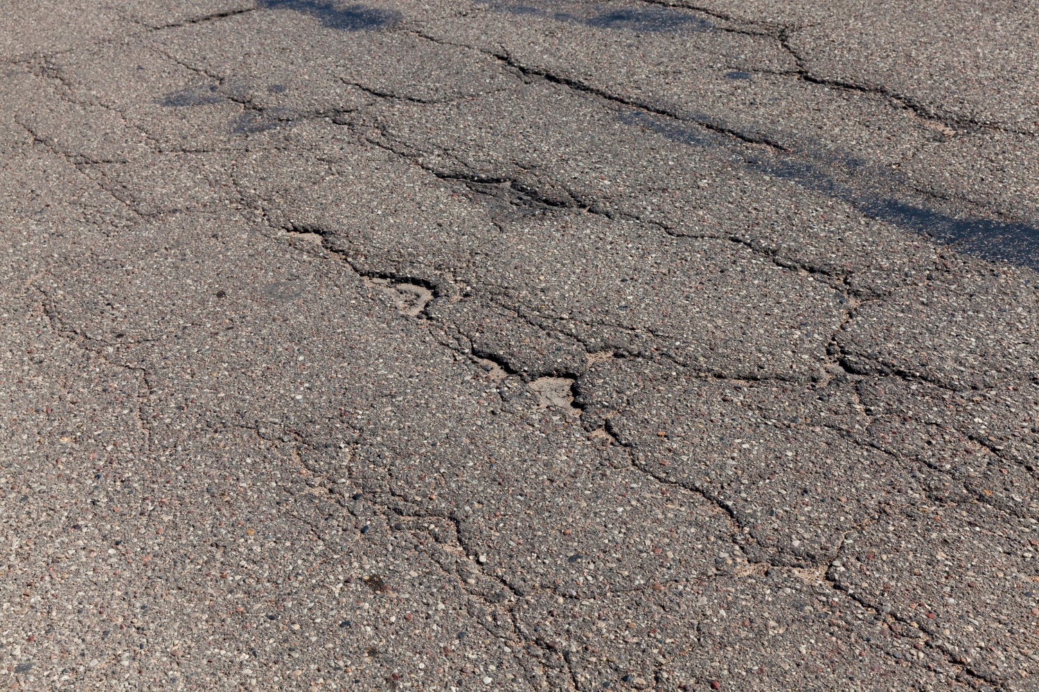 Cracked and damaged asphalt pavement with multiple visible fissures and uneven surface.